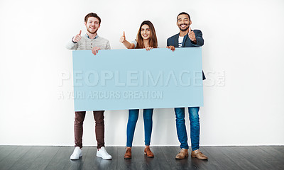 Buy stock photo Studio shot of a group of young people holding a blank placard and showing thumbs up against a white background