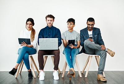 Buy stock photo Shot of a group of young people using wireless technology while sitting in a row