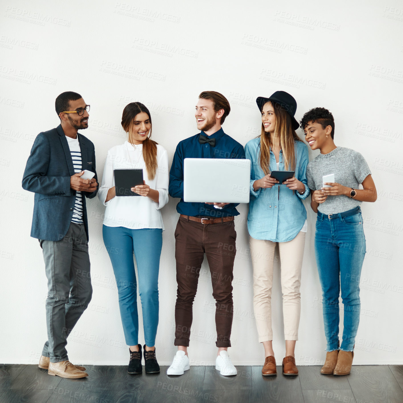 Buy stock photo Business people, waiting room and collaboration with technology in row on a wall background. Young, group or employees with smile on laptop, tablet or phone for job research or career opportunity