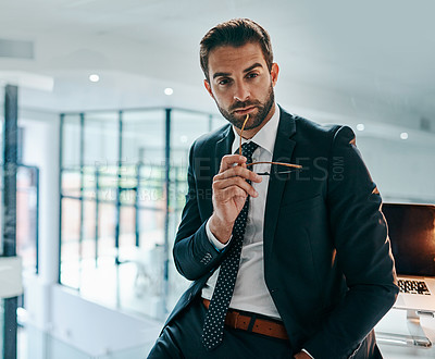 Buy stock photo Portrait of a confident young businessman leaning against his table inside of the office during the day