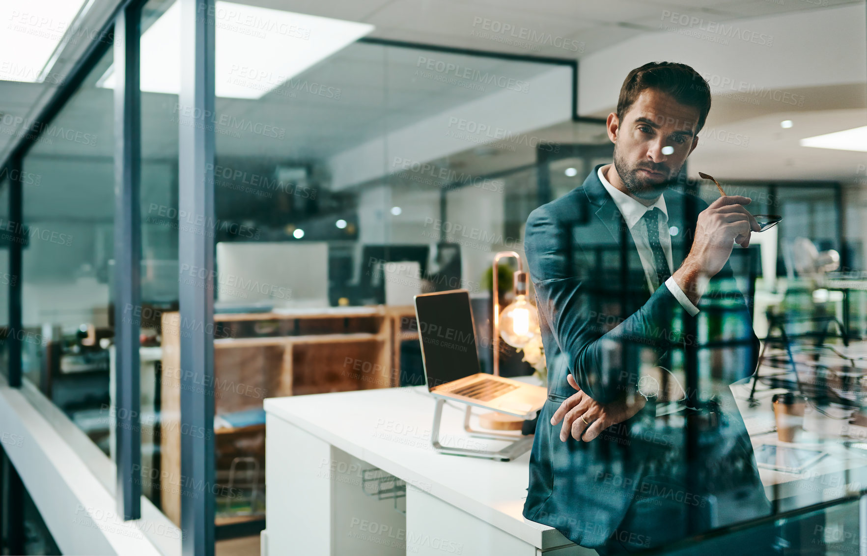 Buy stock photo Portrait of a confident young businessman leaning against his table inside of the office during the day