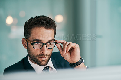 Buy stock photo Shot of a focused young businessman holding his glasses while working on a computer inside of the office