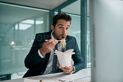 Buy stock photo Shot of a focused young businessman eating noodles while looking on a computer screen inside of the office