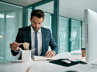 Buy stock photo Shot of a focused young businessman eating noodles while writing in a notebook inside of the office