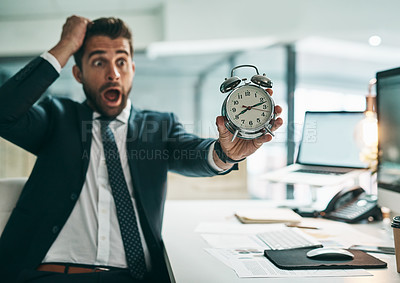 Buy stock photo Shot of a surprised young businessman holding an alarm clock while being seated in the office