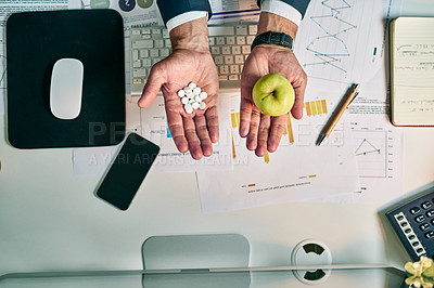 Buy stock photo High angle shot of an unrecognizable businessman holding an apple in one hand and a bunch of pills in the other at the office