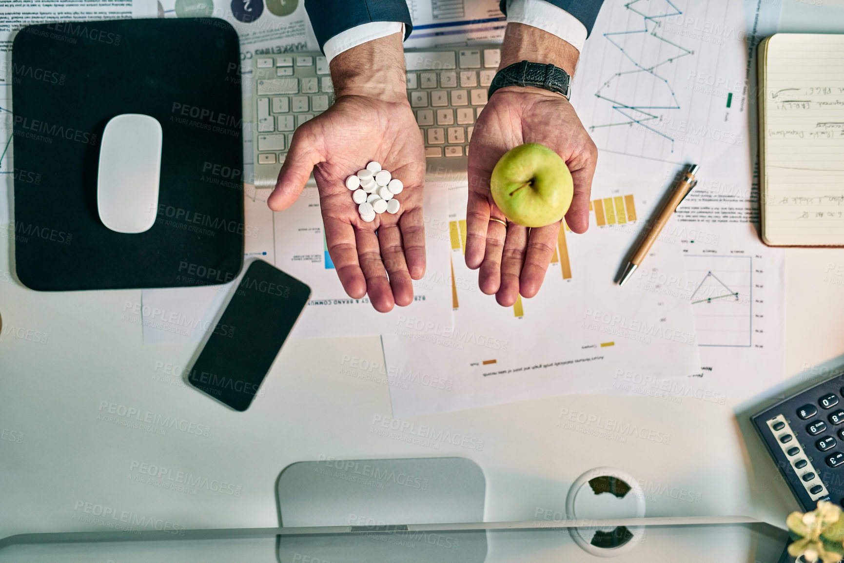 Buy stock photo High angle shot of an unrecognizable businessman holding an apple in one hand and a bunch of pills in the other at the office