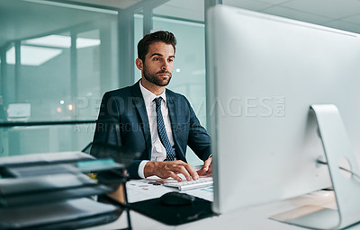 Buy stock photo Shot of a focused young businessman working on his computer and typing while being seated in the office