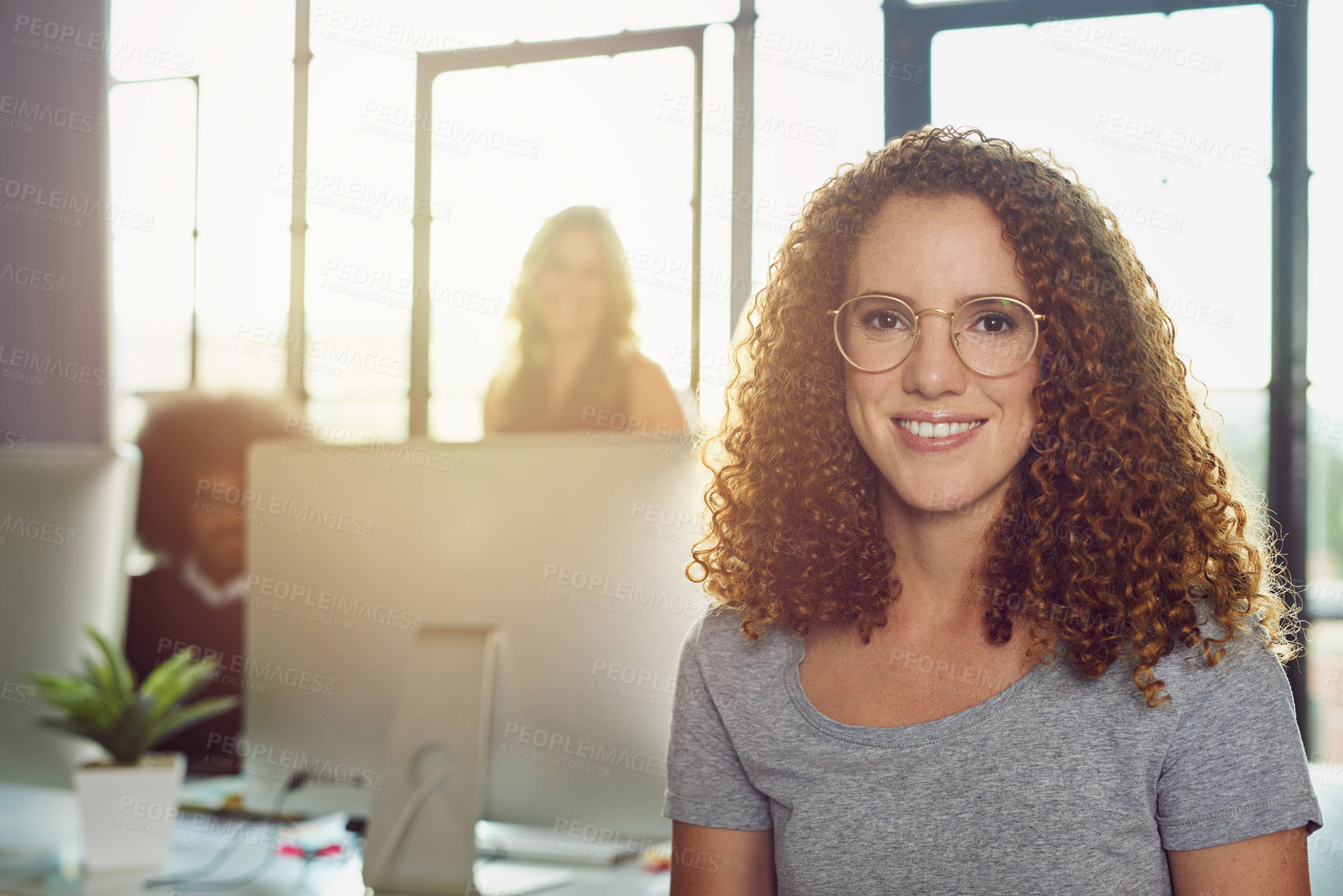 Buy stock photo Portrait of a young designer sitting in an office with her colleagues in the background