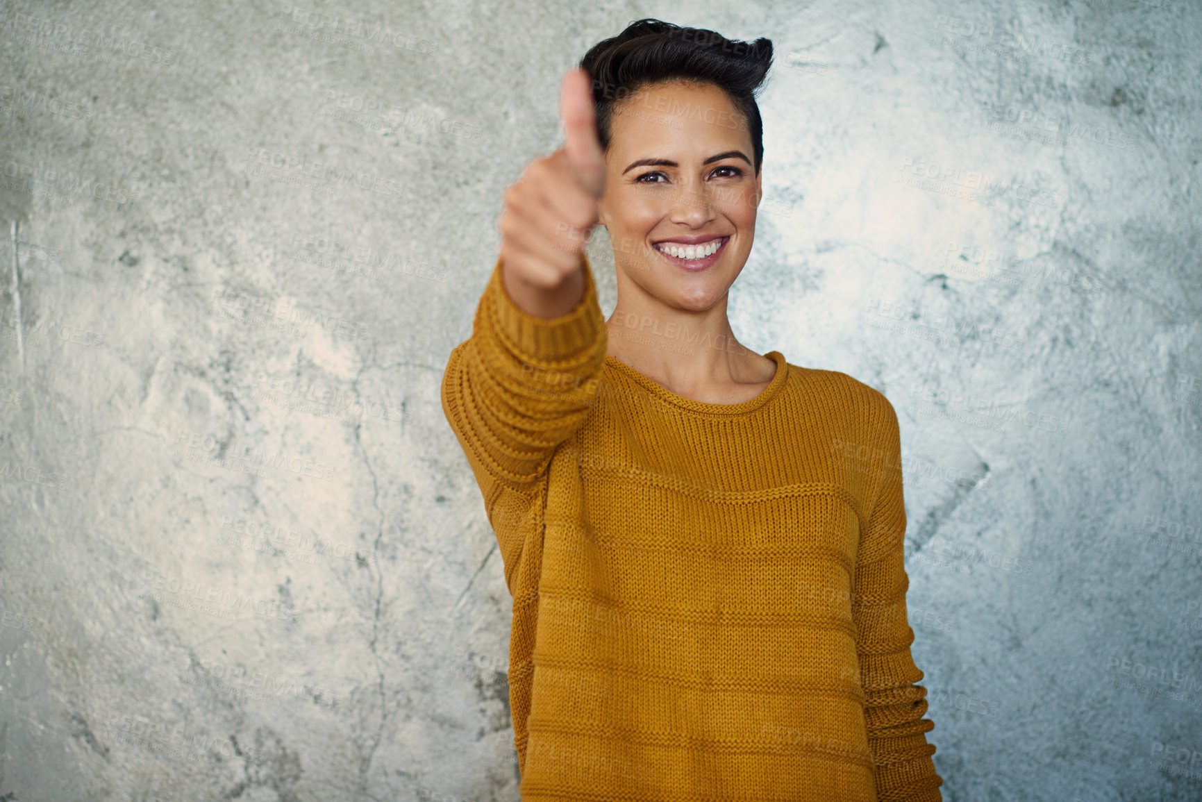 Buy stock photo Portrait of a confident young businesswoman showing thumbs up while standing against a grey wall