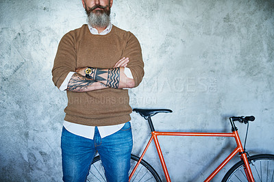Buy stock photo Studio shot of a middle aged man standing with his arms folded with a red bicycle in the back against a grey background
