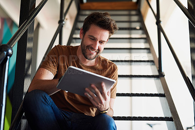 Buy stock photo Shot of a young designer working on his tablet while sitting on a staircase in the office
