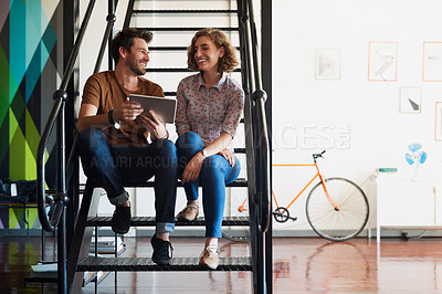 Buy stock photo Shot of two designers discussing something on a tablet while sitting on a staircase