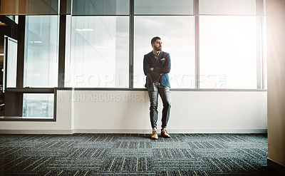 Buy stock photo Shot of a young businessman leaning against a wall and looking thoughtful in a modern office