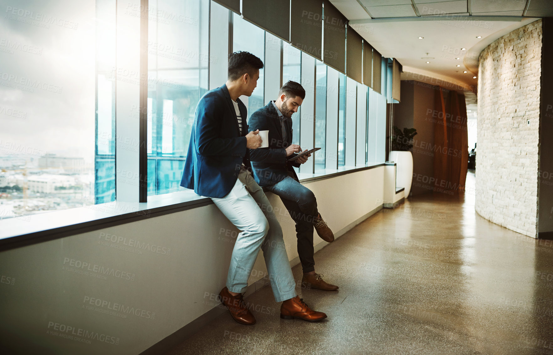 Buy stock photo Shot of a young businessman using a digital tablet while his colleague has his coffee break at work