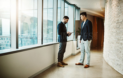 Buy stock photo Shot of two young businessmen using a digital tablet together in a modern office