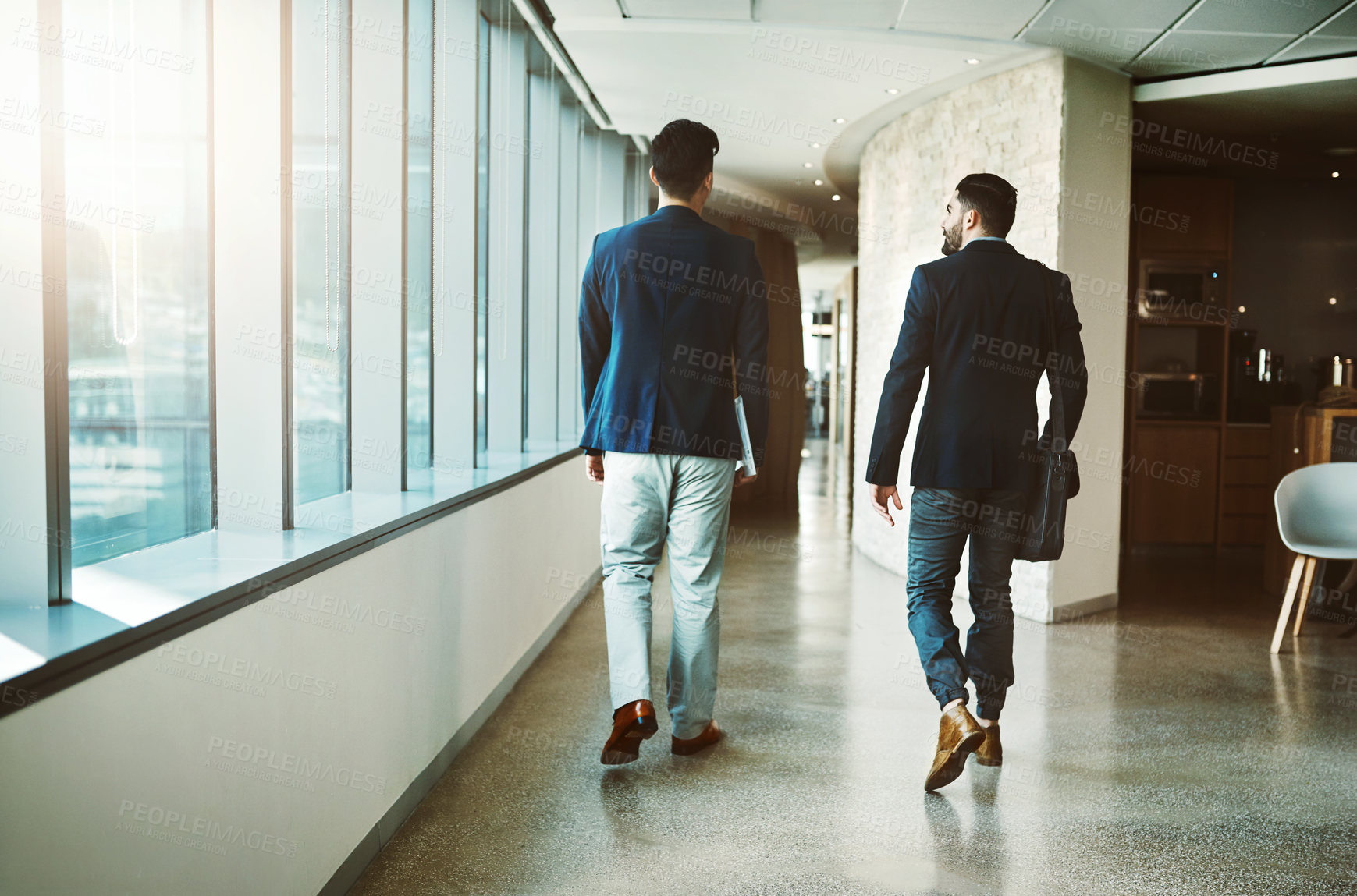 Buy stock photo Rearview shot of two young businessmen walking down a corridor of a modern office