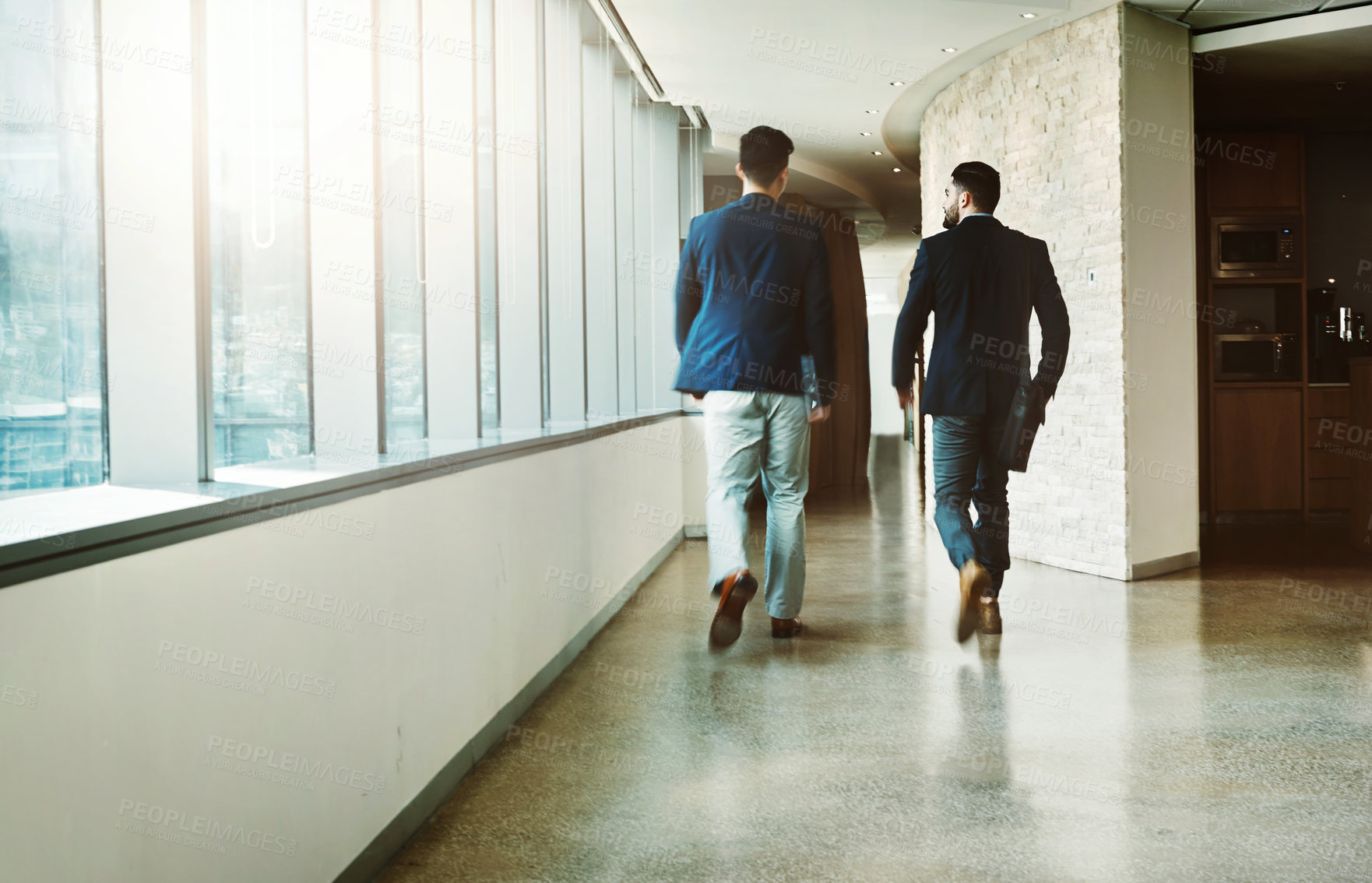 Buy stock photo Rearview shot of two young businessmen walking down a corridor of a modern office