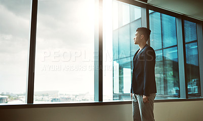 Buy stock photo Shot of a young businessman looking thoughtfully out of an office window