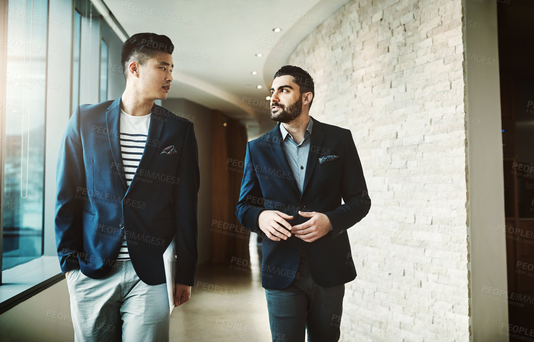 Buy stock photo Shot of two young businessmen walking and talking in a modern office