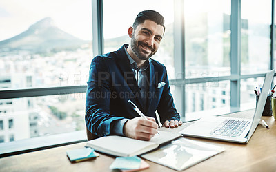 Buy stock photo Portrait of a young businessman writing in a notebook at his desk in a modern office