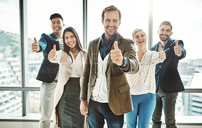 Buy stock photo Portrait of a group of cheerful businesspeople standing together while showing thumbs up to the camera inside of the office