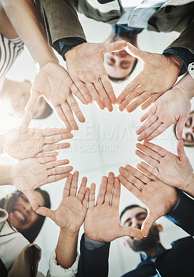 Buy stock photo Low angle shot of a group of cheerful businesspeople forming a huddle with their hands and looking down inside of the office