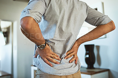 Buy stock photo Hands, back pain and injury with a man standing in the living room of his home, holding his spine in discomfort. Health, medical and anatomy with a male person in a house feeling a muscle cramp