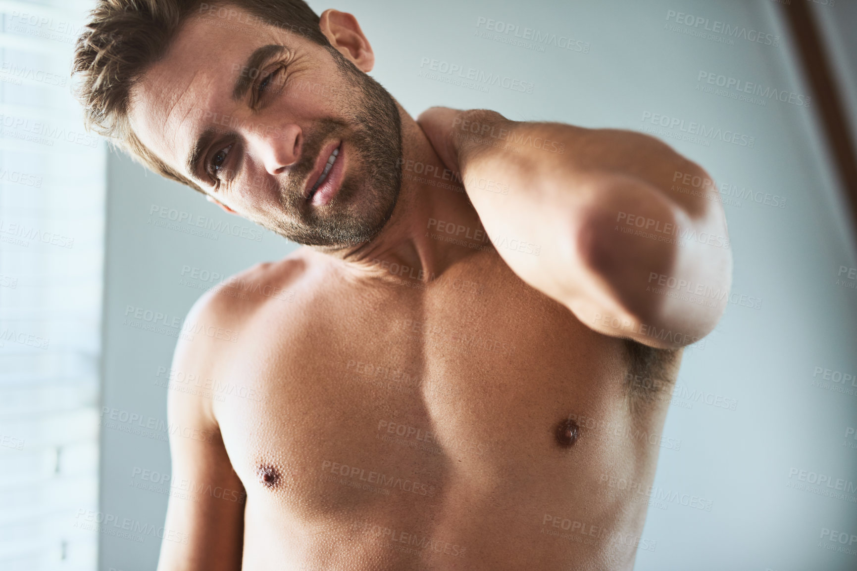 Buy stock photo Shot of an uncomfortable looking shirtless young man holding his neck in discomfort due to pain inside at home