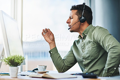 Buy stock photo Shot of a confident young businessman talking through a headset while being seated at his desk in the office