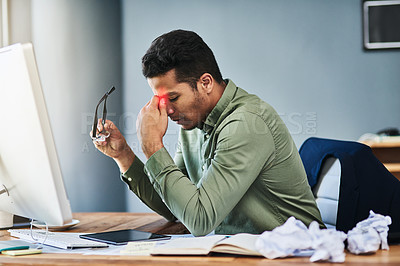 Buy stock photo Shot of a uncomfortable young businessman holding his forehead with his hand in pain while being seated at his desk at the office
