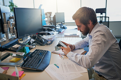 Buy stock photo Shot of a focused young businessman texting on his cellphone while being seated behind his desk in the office