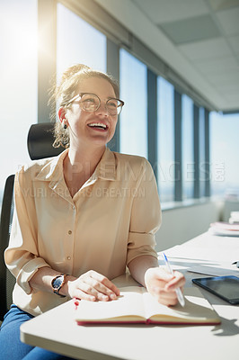 Buy stock photo Shot of a cheerful young businesswoman writing in her notebook while being seated at her desk inside the office during the day