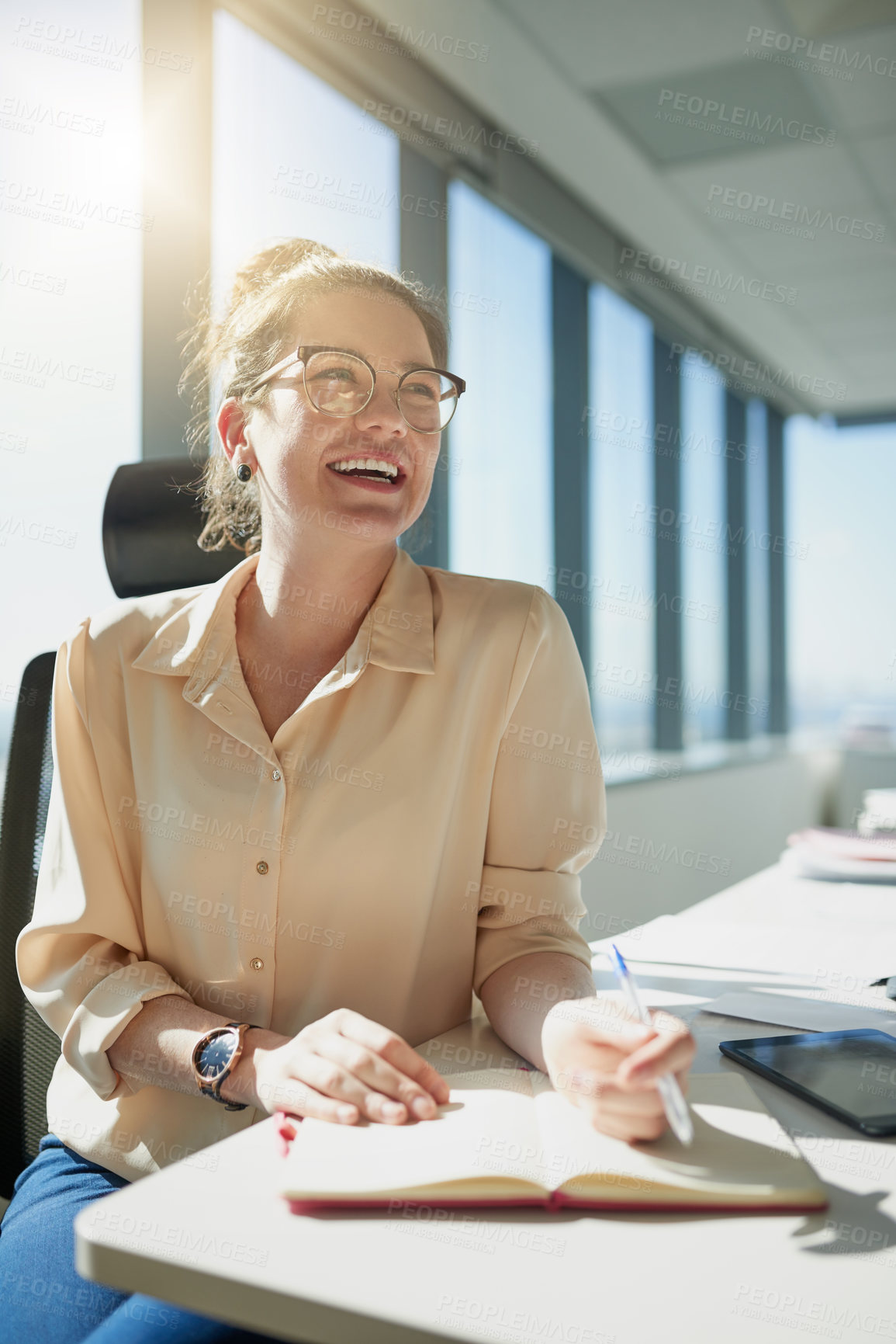 Buy stock photo Shot of a cheerful young businesswoman writing in her notebook while being seated at her desk inside the office during the day