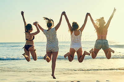 Buy stock photo Rearview shot of female best friends jumping in the air at the beach