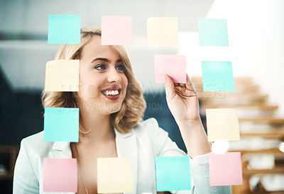 Buy stock photo Shot of a businesswoman arranging sticky notes on a glass wall in a modern office
