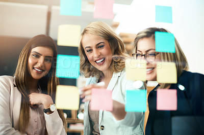 Buy stock photo Shot of a group of businesswomen arranging sticky notes on a glass wall in a modern office