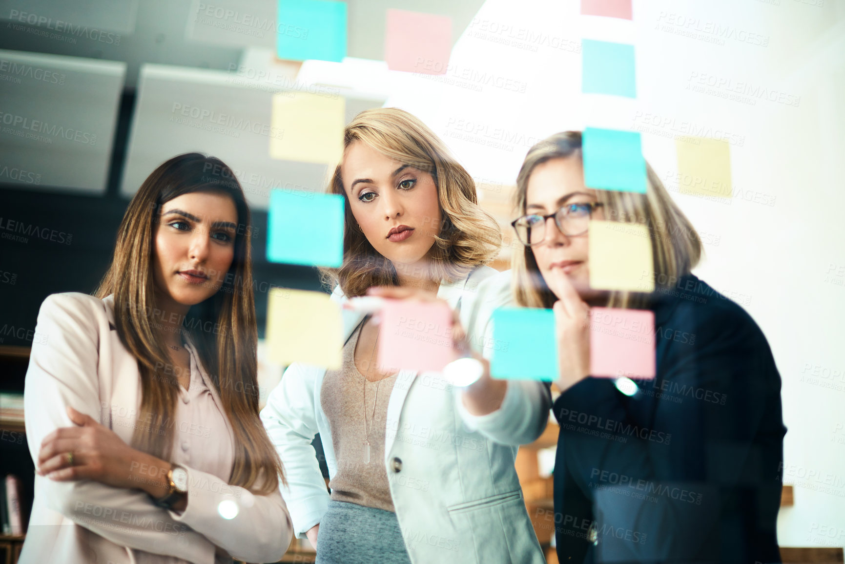 Buy stock photo Talking team leader writing on sticky notes while planning, innovating or sharing business vision or ideas. Diverse group of motivated, ambitious or learning creative business women meeting together