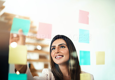 Buy stock photo Shot of a businesswoman arranging sticky notes on a glass wall in a modern office