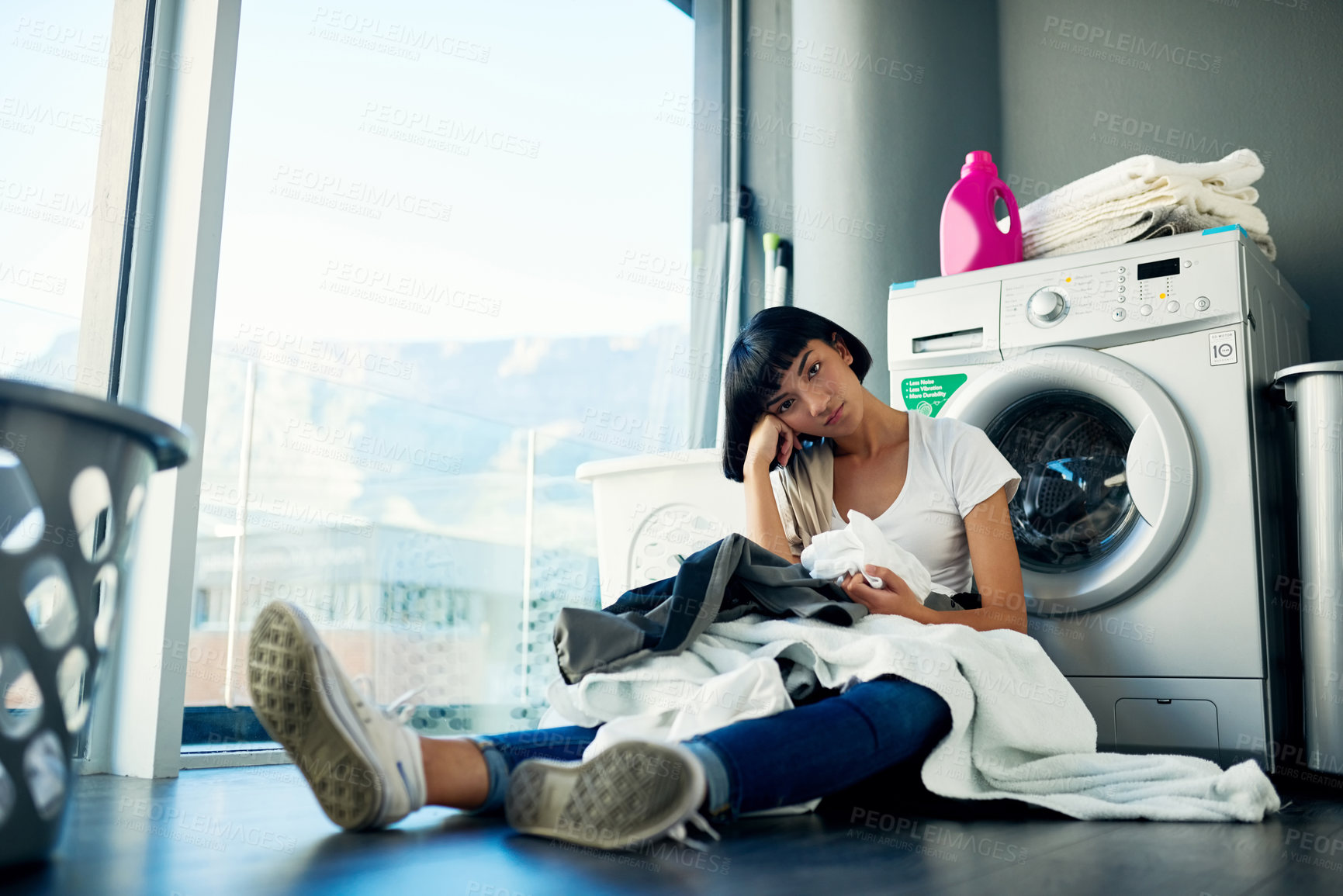 Buy stock photo Shot of an attractive young woman looking bored while doing the laundry at home