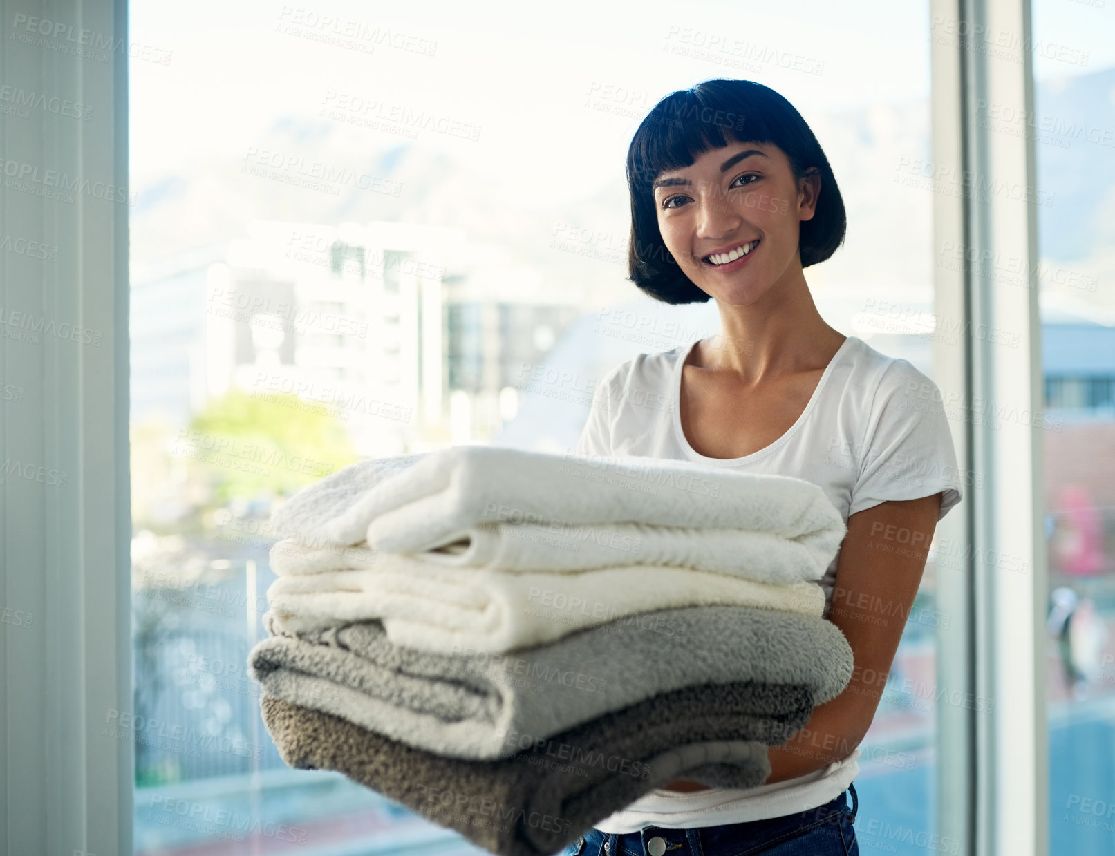 Buy stock photo Cropped shot of a young woman carrying a pile of towels on laundry day at home