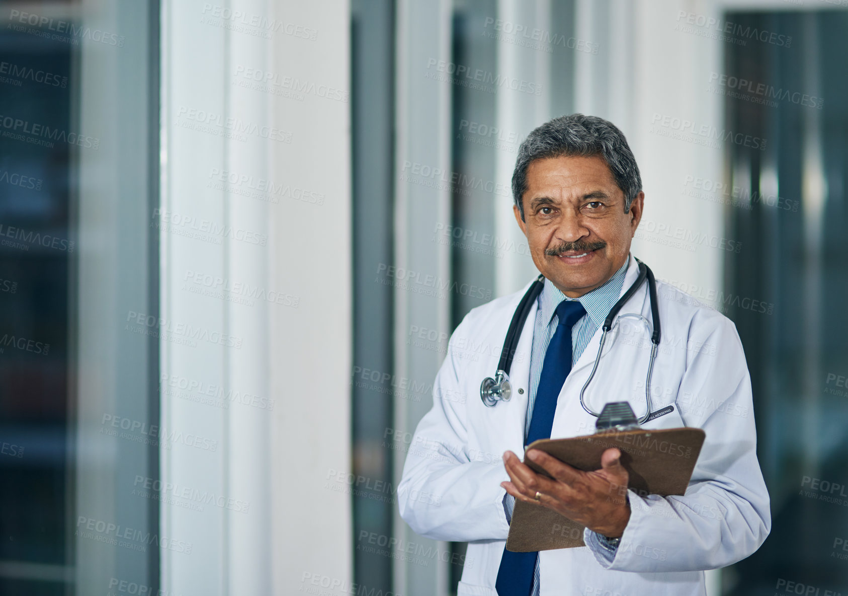 Buy stock photo Portrait of a happy mature doctor holding a clipboard in a hospital