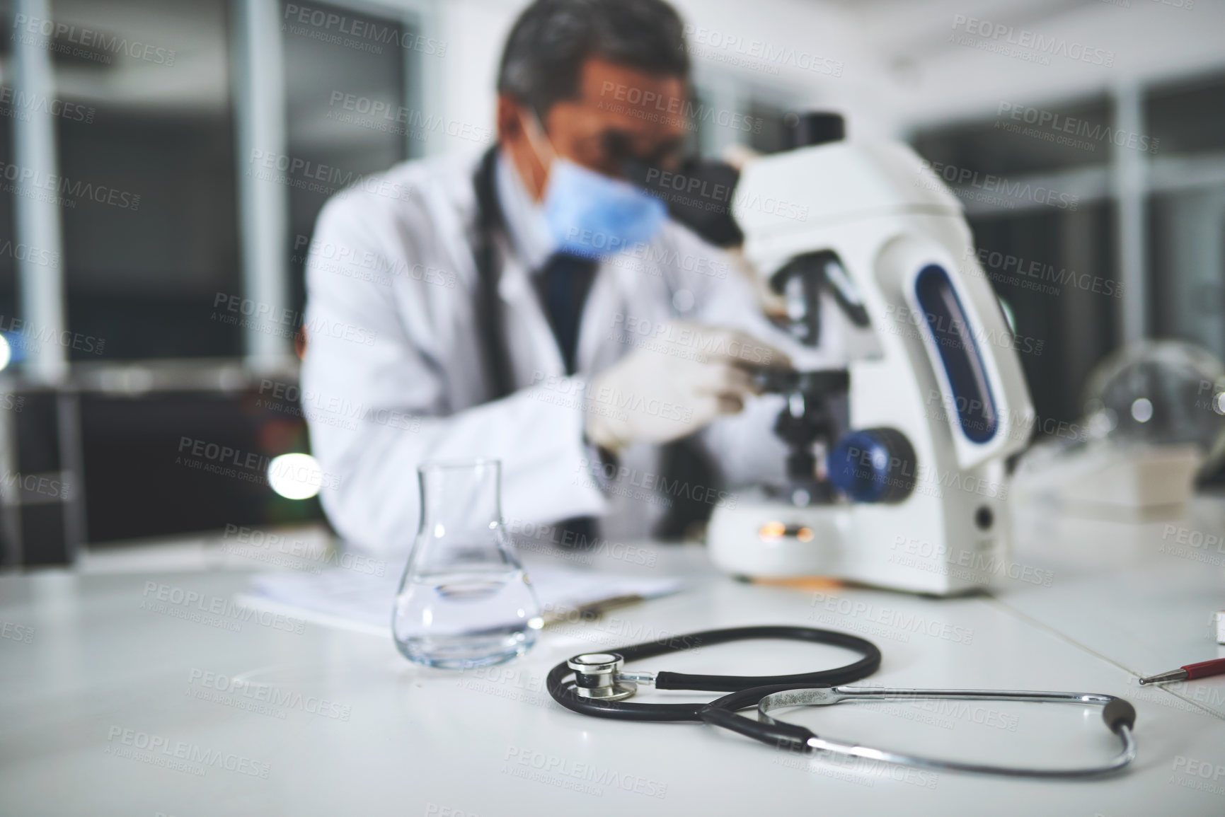 Buy stock photo Shot of a stethoscope on a laboratory table with a scientist using a microscope in the background