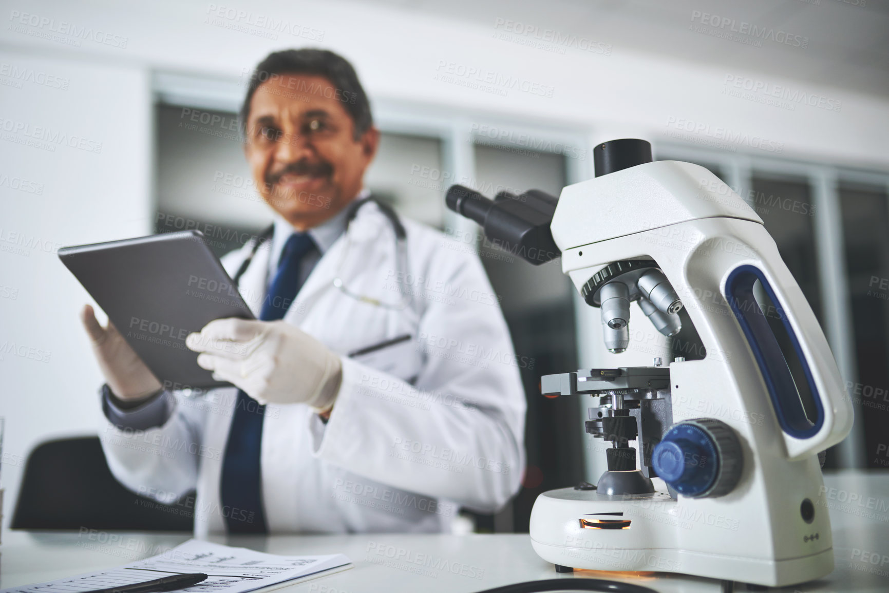 Buy stock photo Shot of a microscope on a laboratory table with a scientist using a digital tablet in the background