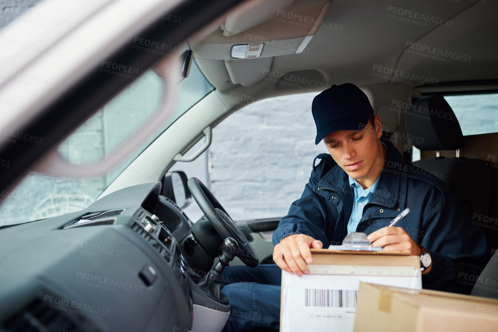Buy stock photo Cropped shot of a handsome young delivery man using a clipboard