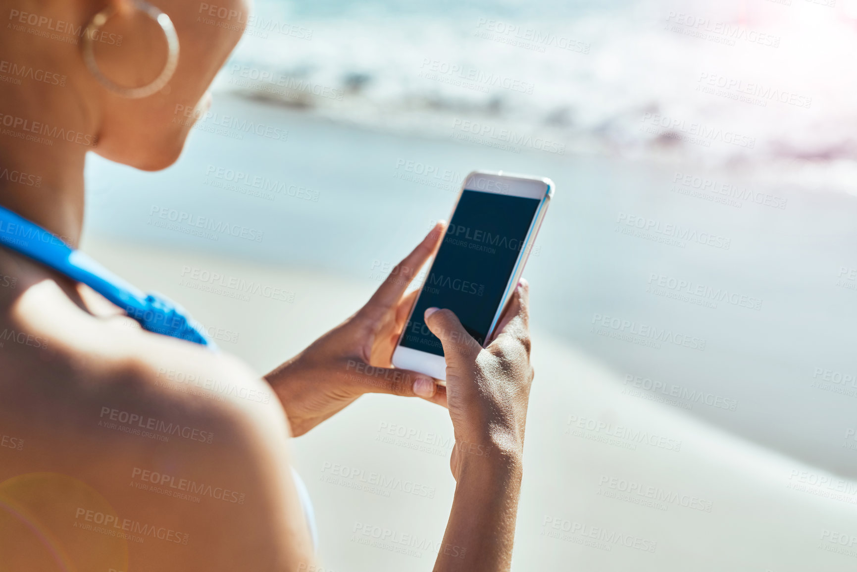 Buy stock photo Cropped shot of a young woman using a mobile phone at the beach