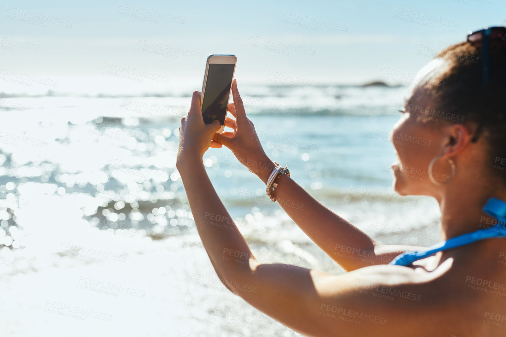 Buy stock photo Shot of a young woman using a mobile phone to take photographs at the beach