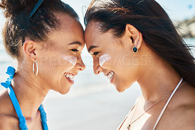 Buy stock photo Shot of two beautiful young women at the beach with sunscreen on their faces smiling at each other