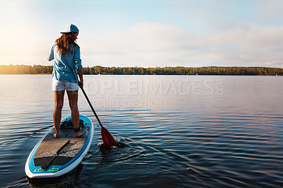 Buy stock photo Shot of a young woman paddle boarding on a lake