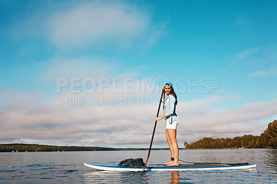 Buy stock photo Shot of a young woman paddle boarding on a lake